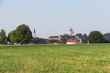 HAAG OBERBAYERN, GERMANY - 19 Haziran 2025: Haag Kalesi 'nin uzak panoramik manzarası ve Yukarı Bavyera' daki açık yaz gökyüzü altında yeşil tarlaların arkasındaki kilise kuleleri. Yüksek kalite fotoğraf