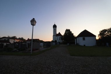 SOYEN, GERMANY - 11 Haziran 2025: Soen Katolik Kilisesi 'nin soğan kubbesi ve çevresindeki köy siluetleri gün batımında çakıl yolundan fotoğraflandı. Yüksek kalite fotoğraf