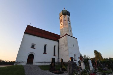 SOYEN, GERMANY - 11 Haziran 2025: Soyen 'deki St. Michael Katolik Kilisesi' nin alacakaranlık manzarası aydınlık cephe ve açık bir akşam gökyüzü altında çevreleyen binalar. Yüksek kalite fotoğraf