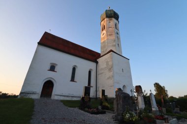 SOYEN, GERMANY - 11 Haziran 2025: Soyen 'deki St. Michael Katolik Kilisesi' nin alacakaranlık manzarası aydınlık cephe ve açık bir akşam gökyüzü altında çevreleyen binalar. Yüksek kalite fotoğraf