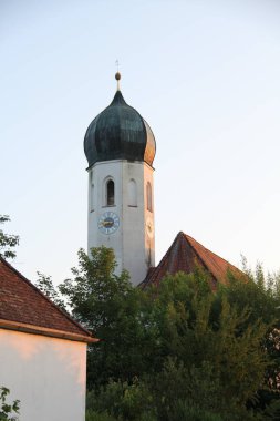 SoYEN, Almanya - 11 Haziran 2025: Güneş batarken Bavyera 'nın Soyen köyünde soğan kubbesi ve ağaçlarla birlikte St. Michael kilise kulesinin yan görüntüsü. Yüksek kalite fotoğraf
