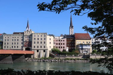 WASSERBURG AM Hanı, ALMANY - 2 Mayıs 2025: Kuleleri, renkli binaları ve ağaç dalları tarafından çerçevelenmiş ahşap köprü ile tarihi kasaba merkezi manzarası. Yüksek kalite fotoğraf