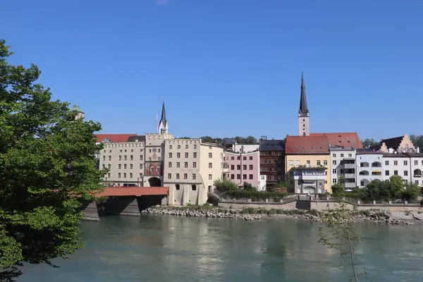 WASSERBURG AM Hanı, GERMANY - 2 Mayıs 2025: Renkli binalar, kilise kuleleri ve açık bir bahar gününde Inn Nehri üzerindeki kırmızı ahşap köprü ile tarihi şehir merkezi manzarası. Yüksek
