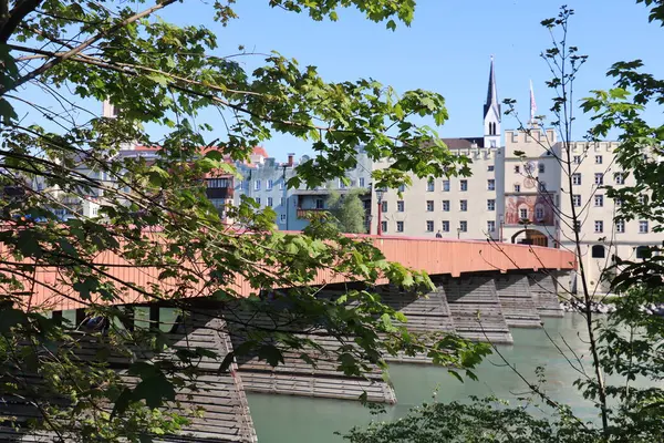 WASSERBURG AM Hanı, ALMANY - 2 Mayıs 2025: Inn Nehri boyunca kilise kulesi olan tarihi ahşap köprünün ve renkli eski kasaba binalarının yeşil yaprakları arasından bakın. Yüksek kalite fotoğraf