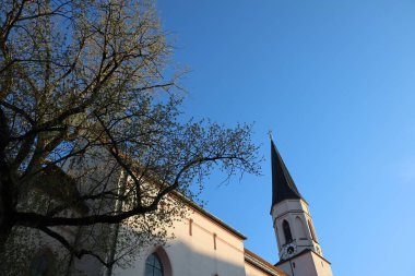 HAAG OBERBAYERN, ALMANY - 28 Nisan 2025: Mariae Himmelfahrt Kilisesi 'nin ağaç dalları ve akşam ışığında açık mavi gökyüzü manzarası. Yüksek kalite fotoğraf
