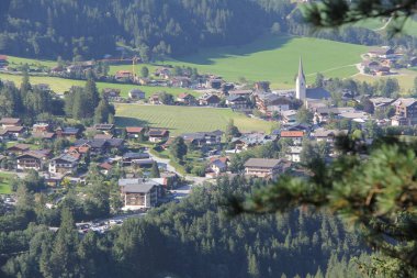 KRIMML, AUSTRIA - 8 AĞUSTRIA: Krimmml köyünün ağaç dalları tarafından çerçevelenmiş kilise kulesi, evler ve çevresindeki alp manzarası ile yüksek görünümü. Yüksek kalite fotoğraf