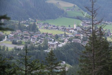 KRIMML, AUSTRIA - 8 AĞUSTRIA: Krimmml köyünün ağaç dalları tarafından çerçevelenmiş kilise kulesi, evler ve çevresindeki alp manzarası ile yüksek görünümü. Yüksek kalite fotoğraf