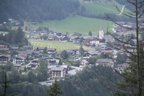 KRIMML, AUSTRIA - 8 AĞUSTRIA: Krimmml köyünün ağaç dalları tarafından çerçevelenmiş kilise kulesi, evler ve çevresindeki alp manzarası ile yüksek görünümü. Yüksek kalite fotoğraf