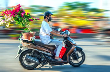 Ho Chi Minh City, Vietnam - 31 Ocak 2022: Vietnamlılar, Vietnam 'ın Ho Chi Minh şehrinde yeni yıl için dekorasyon amaçlı bir evin arkasında elinde çiçek veya kumkuat kabıyla motosiklet kullanıyorlar