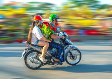 Ho Chi Minh City, Vietnam - 31 Ocak 2022: Vietnamlılar, Vietnam 'ın Ho Chi Minh şehrinde yeni yıl için dekorasyon amaçlı bir evin arkasında elinde çiçek veya kumkuat kabıyla motosiklet kullanıyorlar