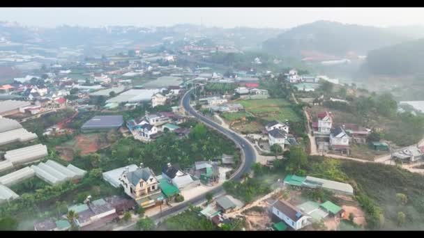 ベトナム高地の霧の多い空と朝のダラット市の近くの玄Tho郊外の空中ビュー 都市開発のテクスチャ 交通インフラ 農業の温室 — ストック動画
