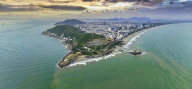 Vung Tau city aerial view with beautiful sunset and so many boats. Panoramic coastal Vung Tau view from above, with waves, coastline, streets, coconut trees and Tao Phung mountain in Vietnam.