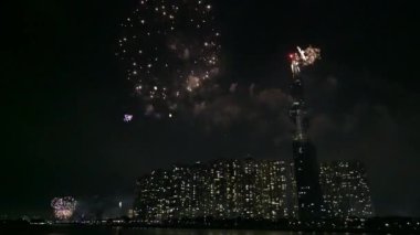 Geceleyin gökyüzünde parlayan renkli havai fişekler nehir kenarı kentsel alanındaki gökdelenin yanında Vietnam 'daki ay yeni yılını karşılıyor.