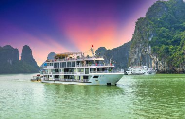 Halong Körfezi, Vietnam 'da rüya gibi bir gün batımı. Kireçtaşı kayaların arasında yüzen turist yolcu gemisi. Burası UNESCO Dünya Mirası Alanı. Kuzey Vietnam 'da çok güzel bir doğa harikası.