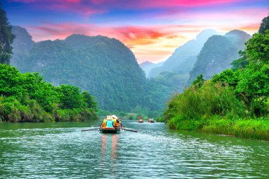 Ninh Binh, Vietnam - 5 Nisan 2024: Turistler Tam Coc Ulusal Parkı turu sırasında tekneyle gün batımında gökyüzü olan mağaralara doğru yüzüyorlar, Ninh Binh, Vietnam.