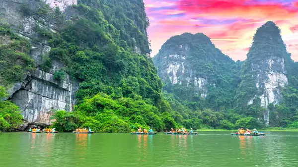 stock image Ninh Binh, Vietnam - April 5th, 2024: Tourists float by boat on the river of the Tam Coc National Park Sightseeing tour to grottoes with sunset sky, Ninh Binh, Vietnam.