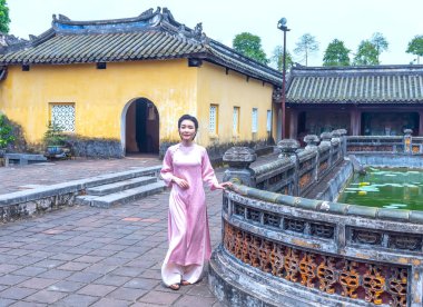 Hue, Vietnam - April 10th, 2024: Hue girl in traditional ao dai walking in the Forbidden City in Hue, Vietnam clipart