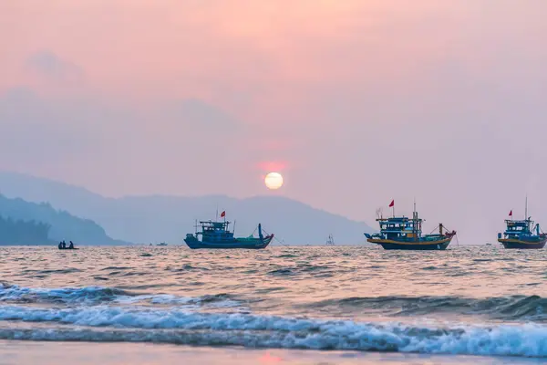 stock image Da Nang, Vietnam - April 15th, 2024: Beach landscape at dawn with silhouettes of fishing boats, mountains and sky at beach. Peaceful life concept, travel.