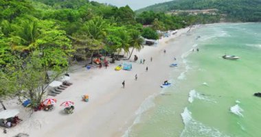 Vietnam 'da uçan insansız hava aracı Sao adası üzerinde uçuyor, beyaz kum, kristal berrak mavi turkuaz su, yeşil palmiye ağaçları ve güneşli bir günde yürüyen insanlar.