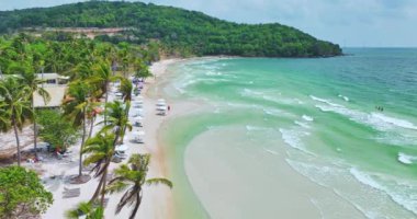 Vietnam 'da uçan insansız hava aracı Sao adası üzerinde uçuyor, beyaz kum, kristal berrak mavi turkuaz su, yeşil palmiye ağaçları ve güneşli bir günde yürüyen insanlar.