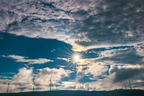Gün batımında mavi bulutlu gökyüzünün altındaki dağlardaki rüzgar türbinlerinin güzel manzarası.