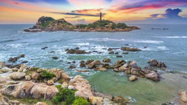 Deniz sahilinde gün batımı, ön planda kayalar.