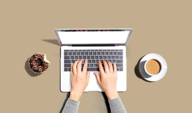 Dizüstü bilgisayarı donut ve bir fincan kahveyle kullanan biri.