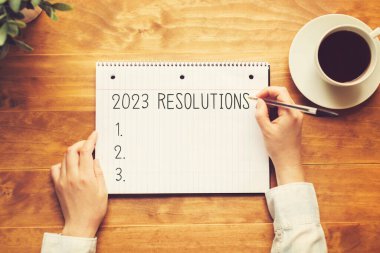 2023 Resolutions with a person holding a pen on a wooden desk clipart