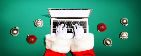 stock image Santa Claus using a laptop computer with Christmas baubles from above