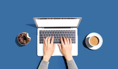 Dizüstü bilgisayarı donut ve bir fincan kahveyle kullanan biri.