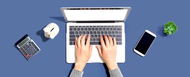 Kumbarası ve hesap makinesi olan dizüstü bilgisayar kullanan bir kadın.