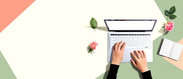 Woman using her laptop with pink roses - flat lay