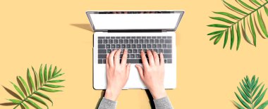 Yukarıdan gelen tropikal yapraklı bir dizüstü bilgisayar kullanan kişi