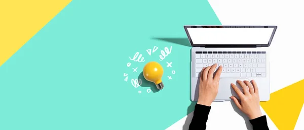 Person using a laptop computer and a light bulb - Flat lay