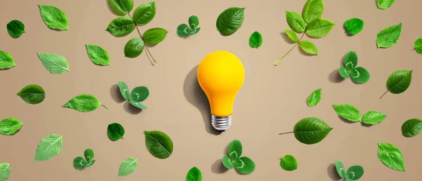 Yellow light bulb with green leaves - Flat lay