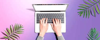 Yukarıdan gelen tropikal yapraklı bir dizüstü bilgisayar kullanan kişi