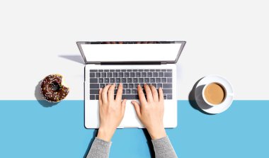 Dizüstü bilgisayarı donut ve bir fincan kahveyle kullanan biri.