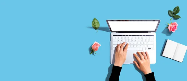 Woman using her laptop with pink roses - flat lay