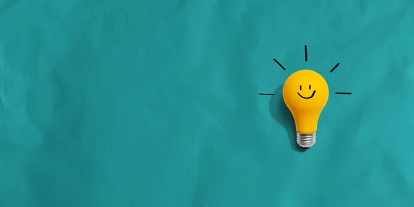 Yellow light bulb with happy face - flat lay