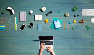 Ofis malzemelerinin olduğu bir dizüstü bilgisayar kullanan kişi.