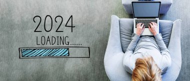 Yeni yıl 2024 'ü modern gri sandalyede dizüstü bilgisayar kullanan bir adamla doldurmak