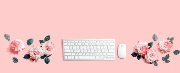 Computer keyboard and a mouse with pink roses - flat lay