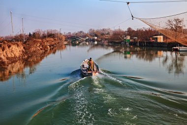 Ravenna, Emilia Romagna, İtalya: doğadaki sulak arazinin manzarası Po Delta Parkı, nehirde balıkçı kulübeleri ve teknede balıkçılar