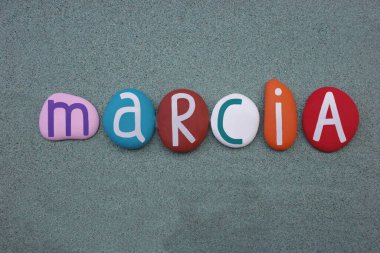 Marcia, female given name composed with multi colored stone letters over green sand