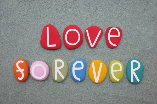 Love forever, creative message composed with multi colored stone letters over green sand