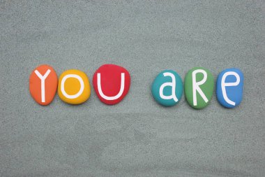 Sen, yeşil kumların üzerinde çok renkli taş harflerle oluşturulmuş yaratıcı bir metinsin.