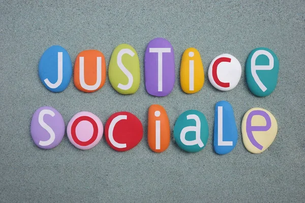 Justice Social, french phrase meaning Social Justice composed with multi colored stone letters over green sand