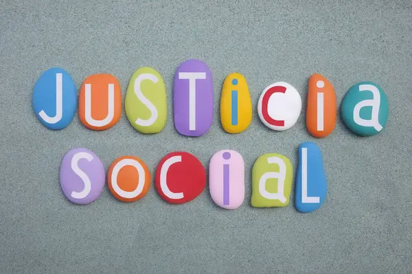 Justicia Social, spanish phrase meaning Social Justice composed with multi colored stone letters over green sand