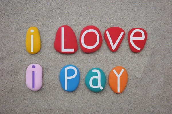 I love, I pay, funny slogan composed with hand painted multi colored stone letters over brown sand