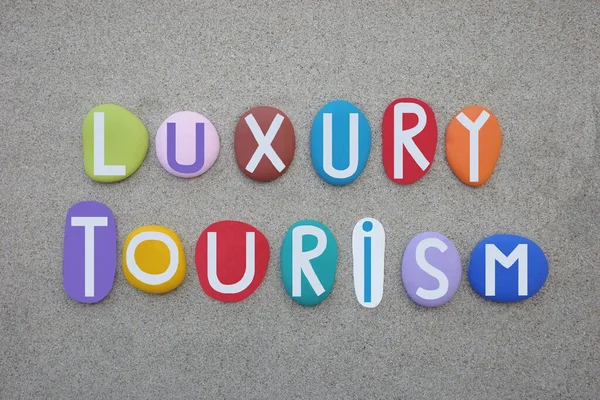 Luxury Tourism, creative logo composed with hand painted multi colored stone letters over beach sand